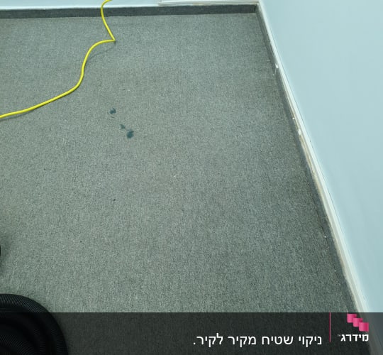 שטיח אפור עם כתמים, כבל חשמל צהוב ושואב אבק